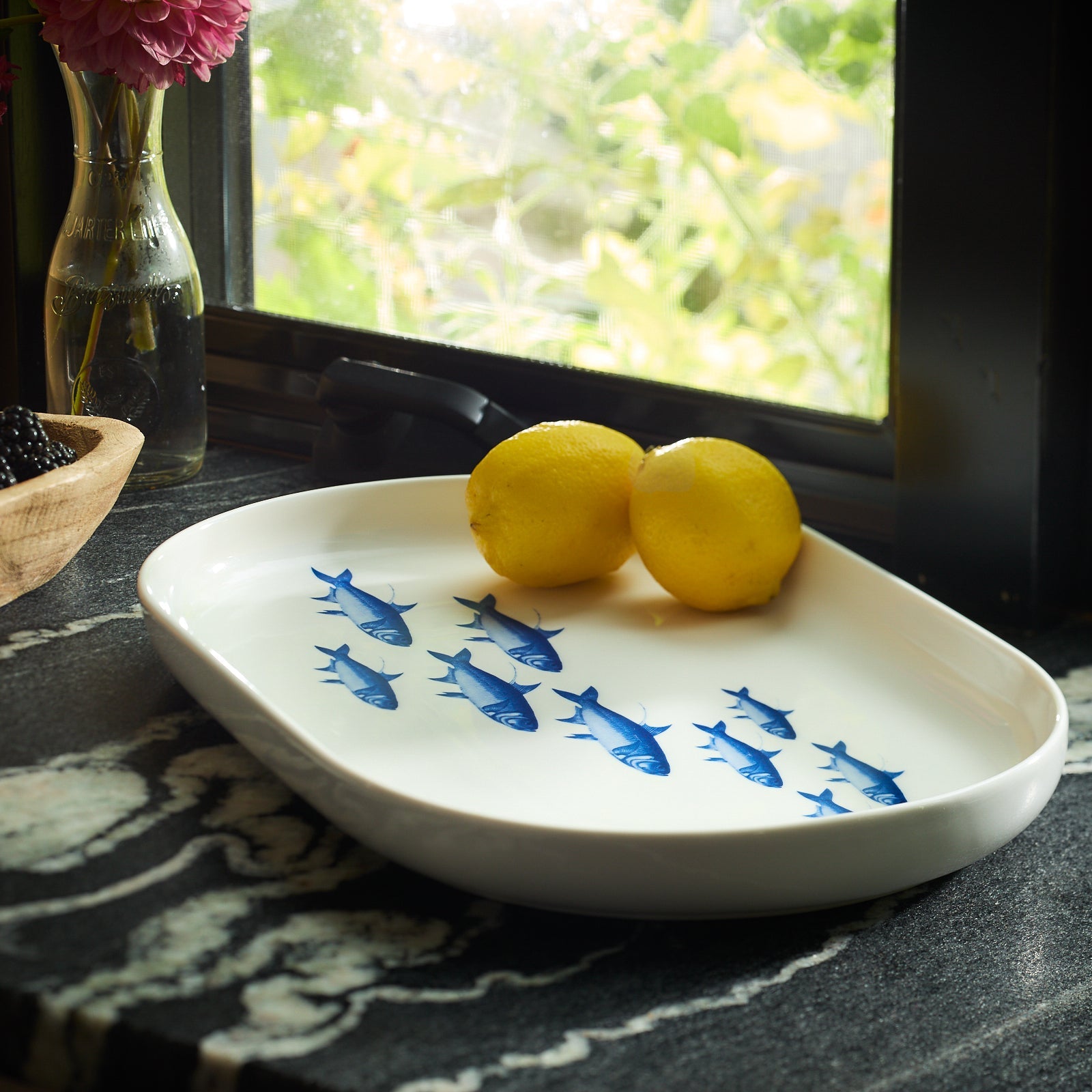 white platter with blue fish with two lemons on a black marble counter