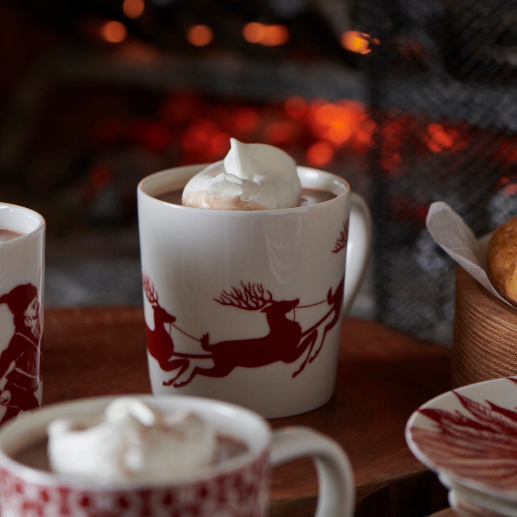 white mug with red reindeer filled with hot chocolate with whipped cream on top 