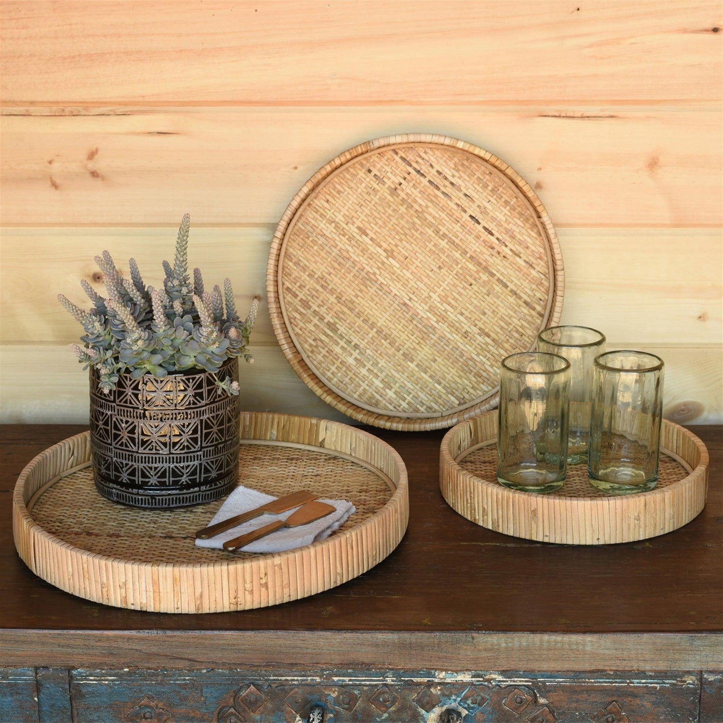 three round rattan trays with glasses and a plant