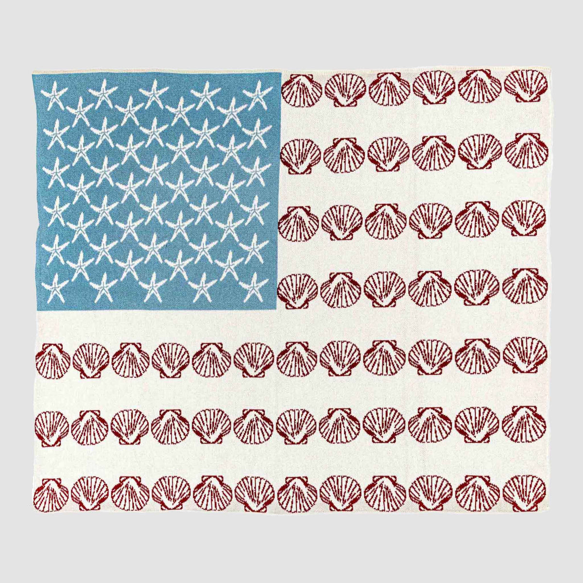 	Coastal Flag knit throw laid flat with white starfish on blue and rows of red seashells forming an American flag-inspired design