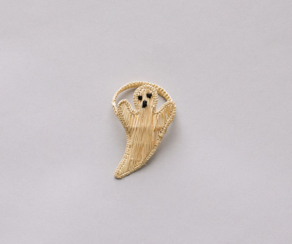 Woven straw ghost-shaped decoration with a circular handle on a light gray background.