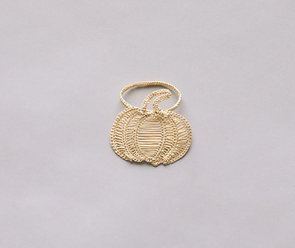 Woven decorative pumpkin in natural tones, resting on a neutral gray background.