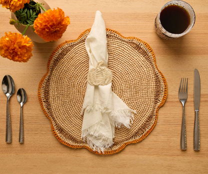 Table setting featuring a woven placemat, white napkin, marigolds, and coffee cup.
