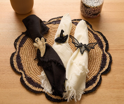 Three napkins with Halloween-themed holders rest on a woven placemat.