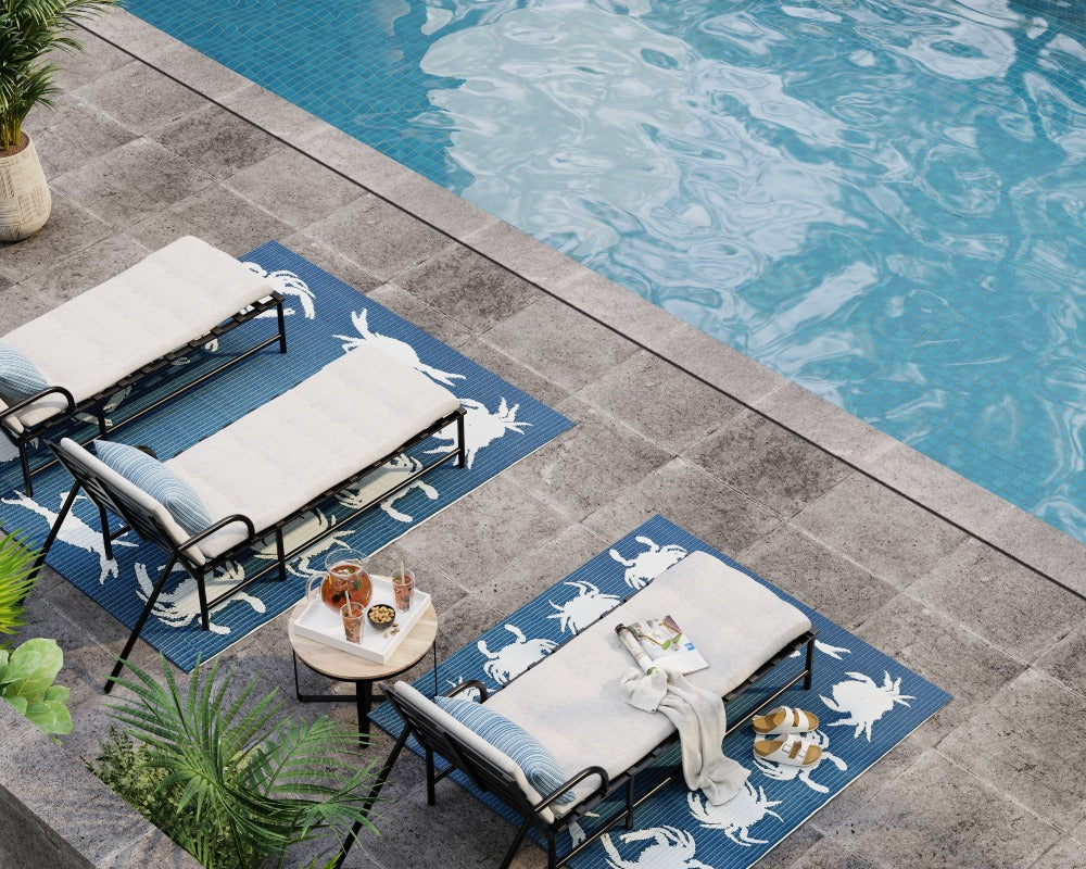 Two blue crab-pattern rugs styled beneath lounge chairs beside a swimming pool