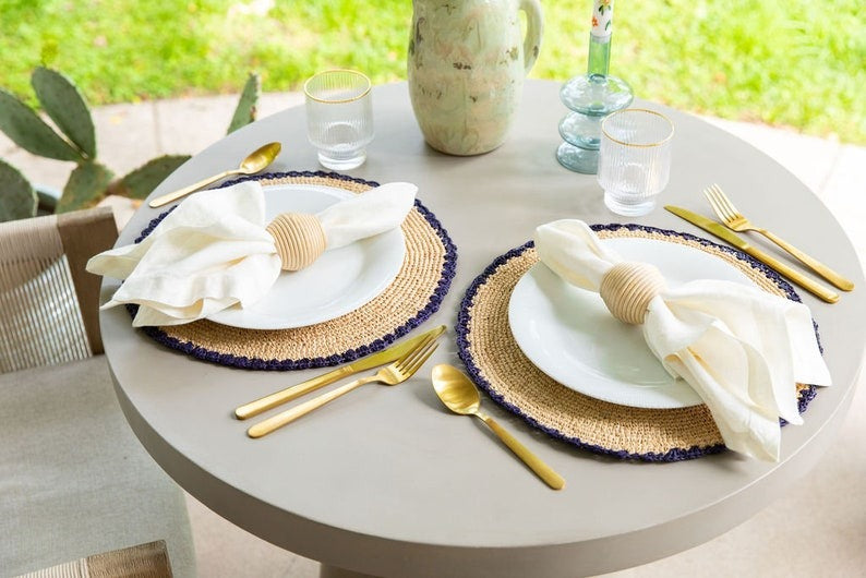 Round table set with white plates, gold cutlery, and decorative napkins on a patio.