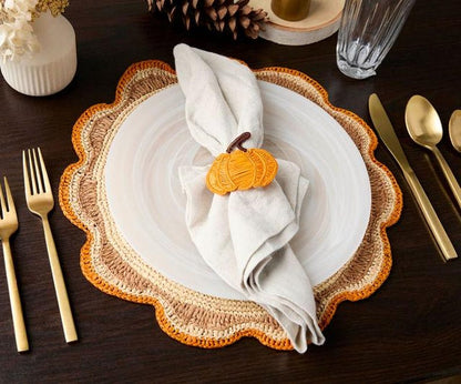 Decorative table setting with a plate, gold utensils, and a napkin held by a pumpkin-shaped holder.