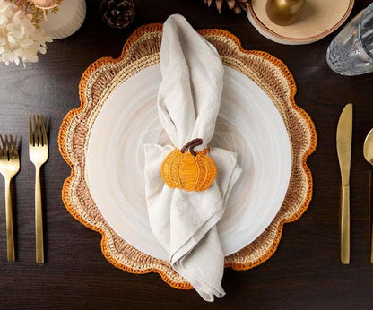 Table setting with a plate, orange pumpkin napkin holder, and gold utensils on a dark wood surface.