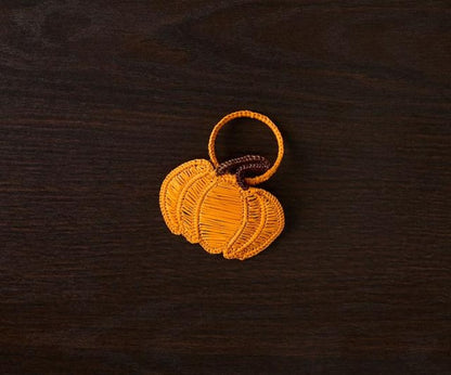 Orange woven pumpkin keychain on a dark wooden surface.