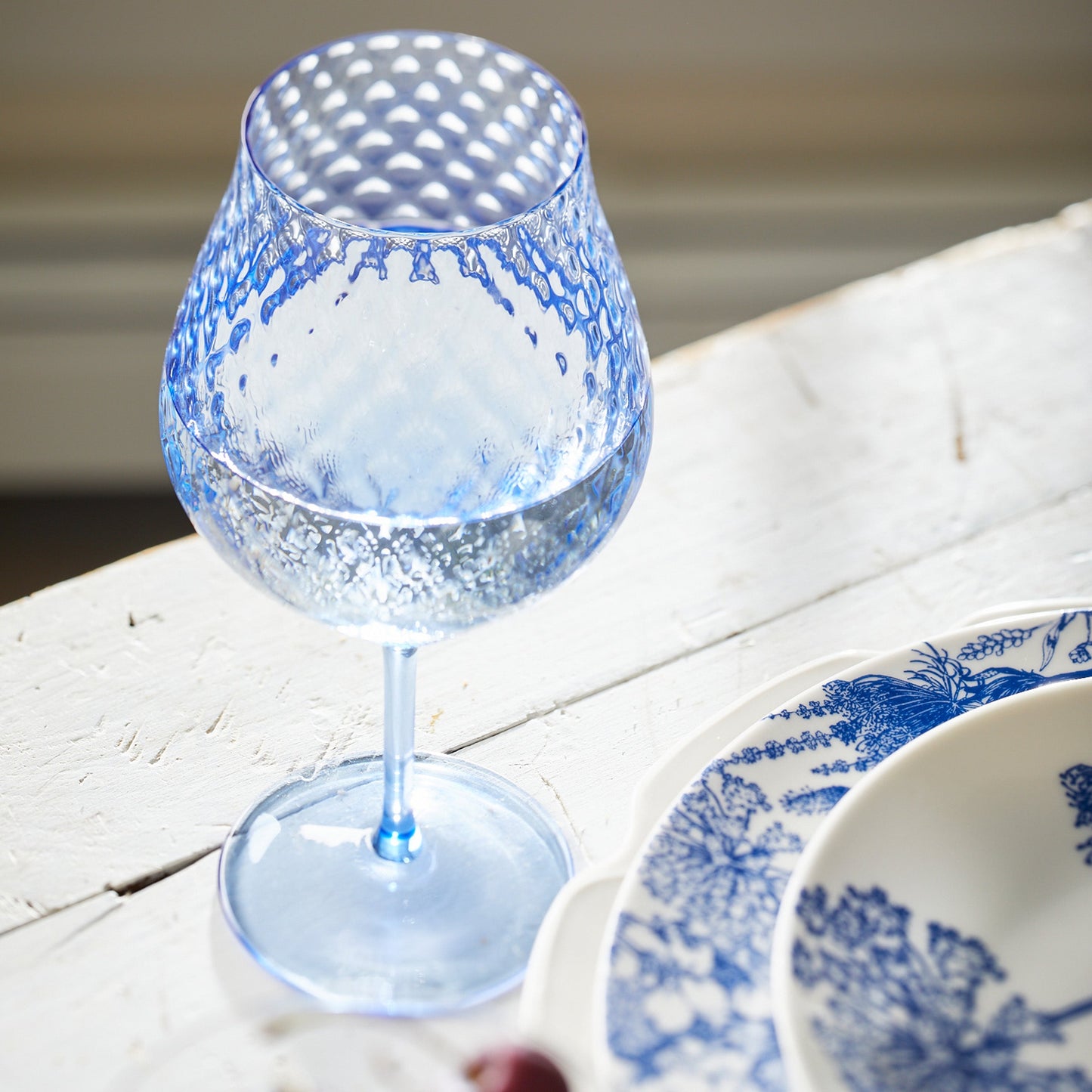 blue wine glass on white table next to blue plates