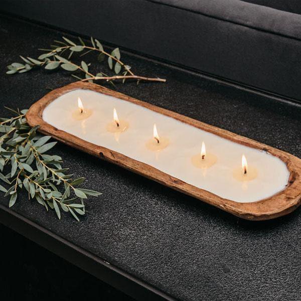 wood dough bowl with white candle on a table with greenery