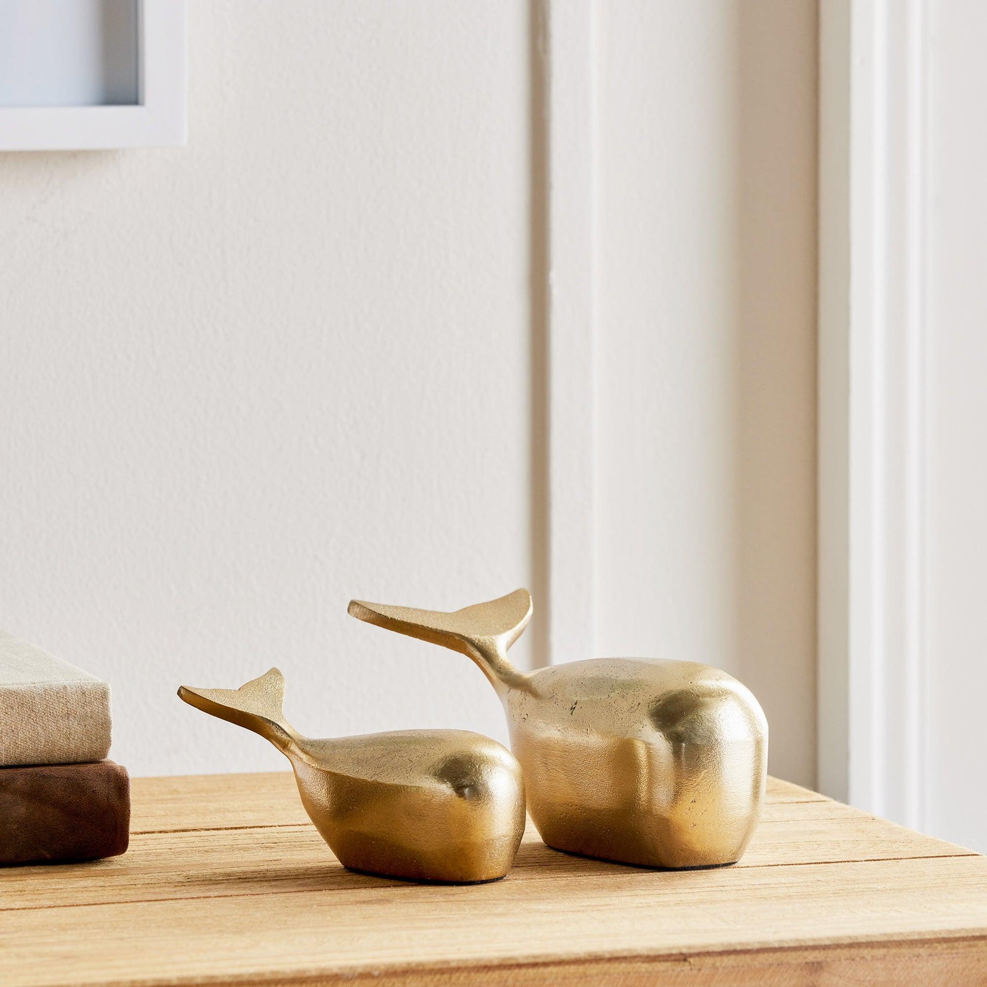 a pair of brass whale decor objects on a wood table 