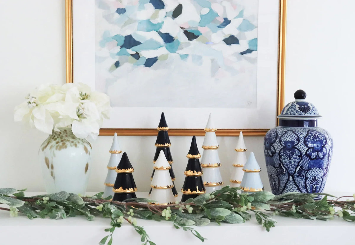 Navy and white tiered Christmas trees with gold trim styled with greenery and a blue-and-white ginger jar