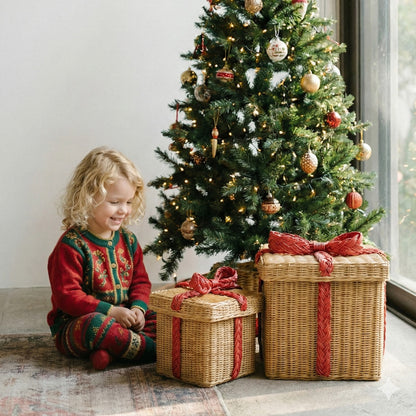 	Child beside two natural rattan storage gift boxes with red bows beneath a decorated Christmas tree