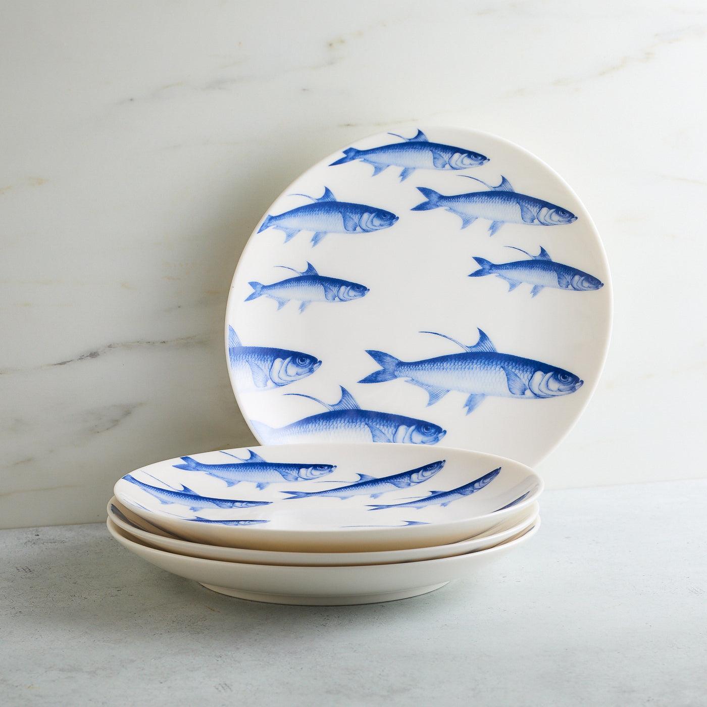 a set of four blue and white plates with fish on them