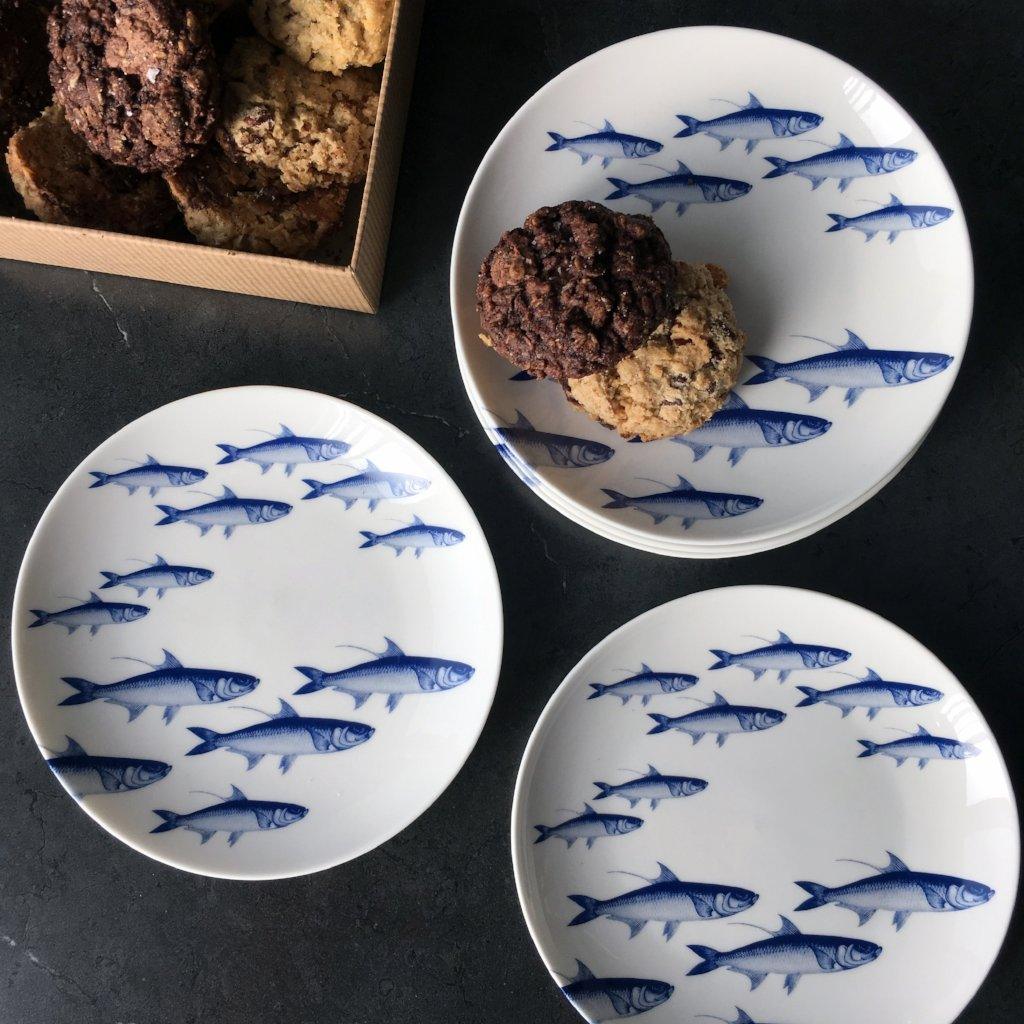 three plates with blue fish on them next to a box of cookies