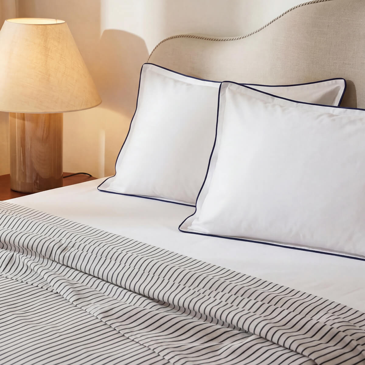 Porto striped top sheet folded back beneath white pillowcases with midnight blue piping