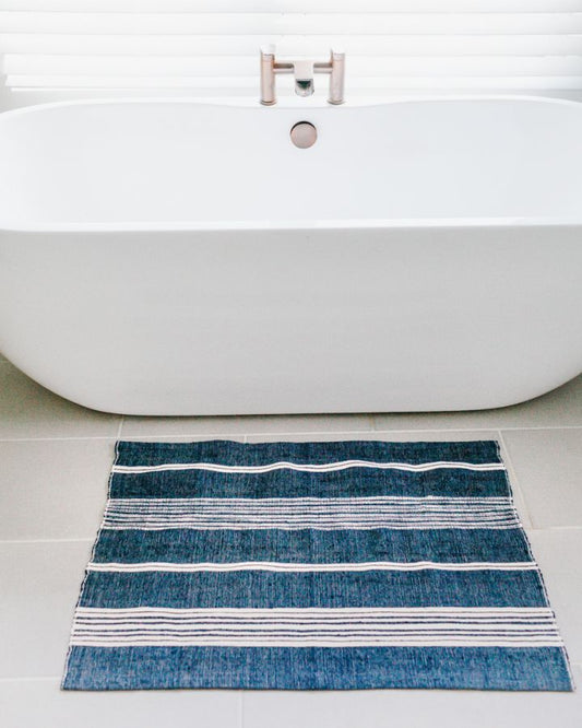 navy and white striped bath mat in front of white bathtub