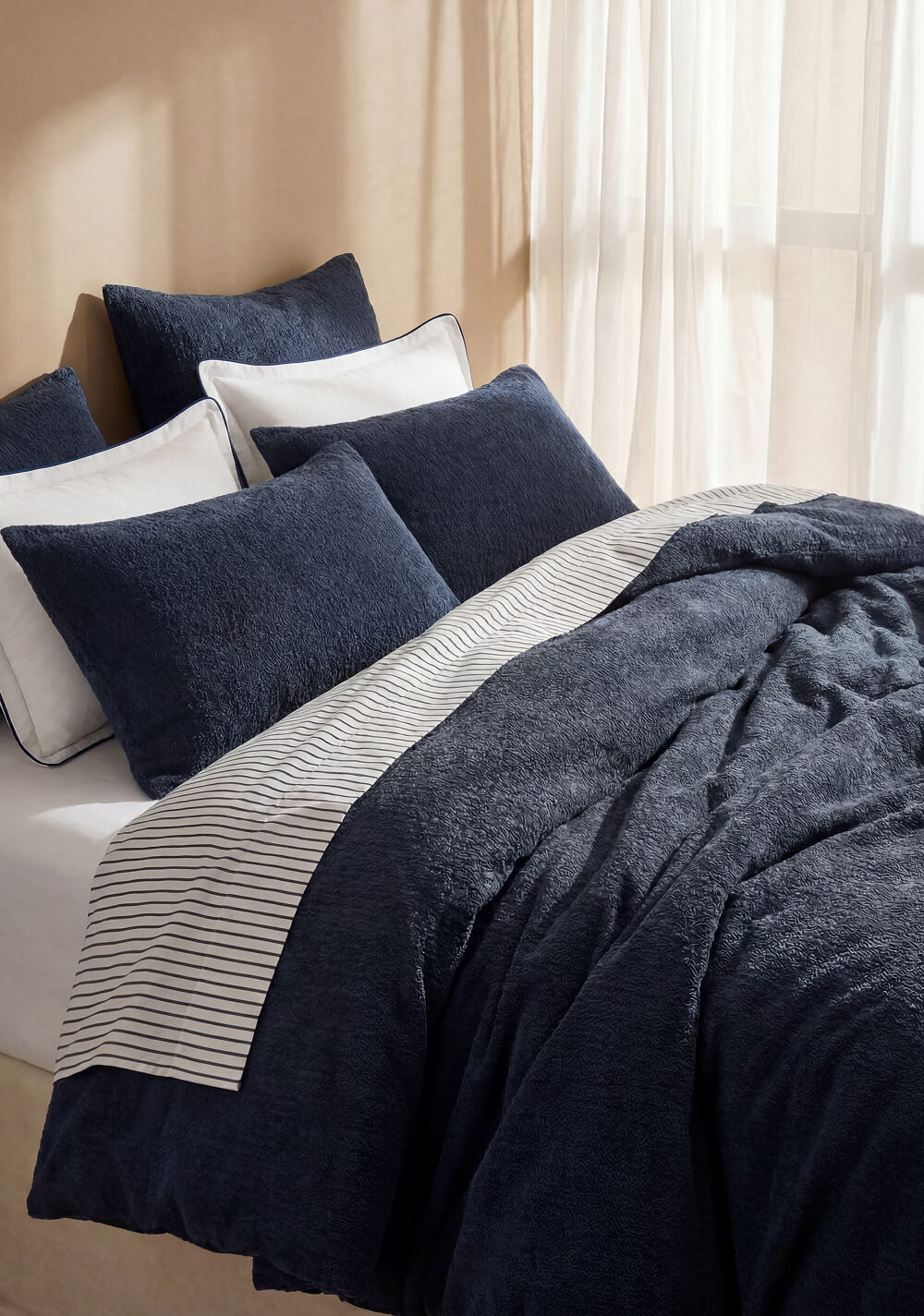 Porto blue-trimmed white pillowcases styled with navy bedding and a striped top sheet