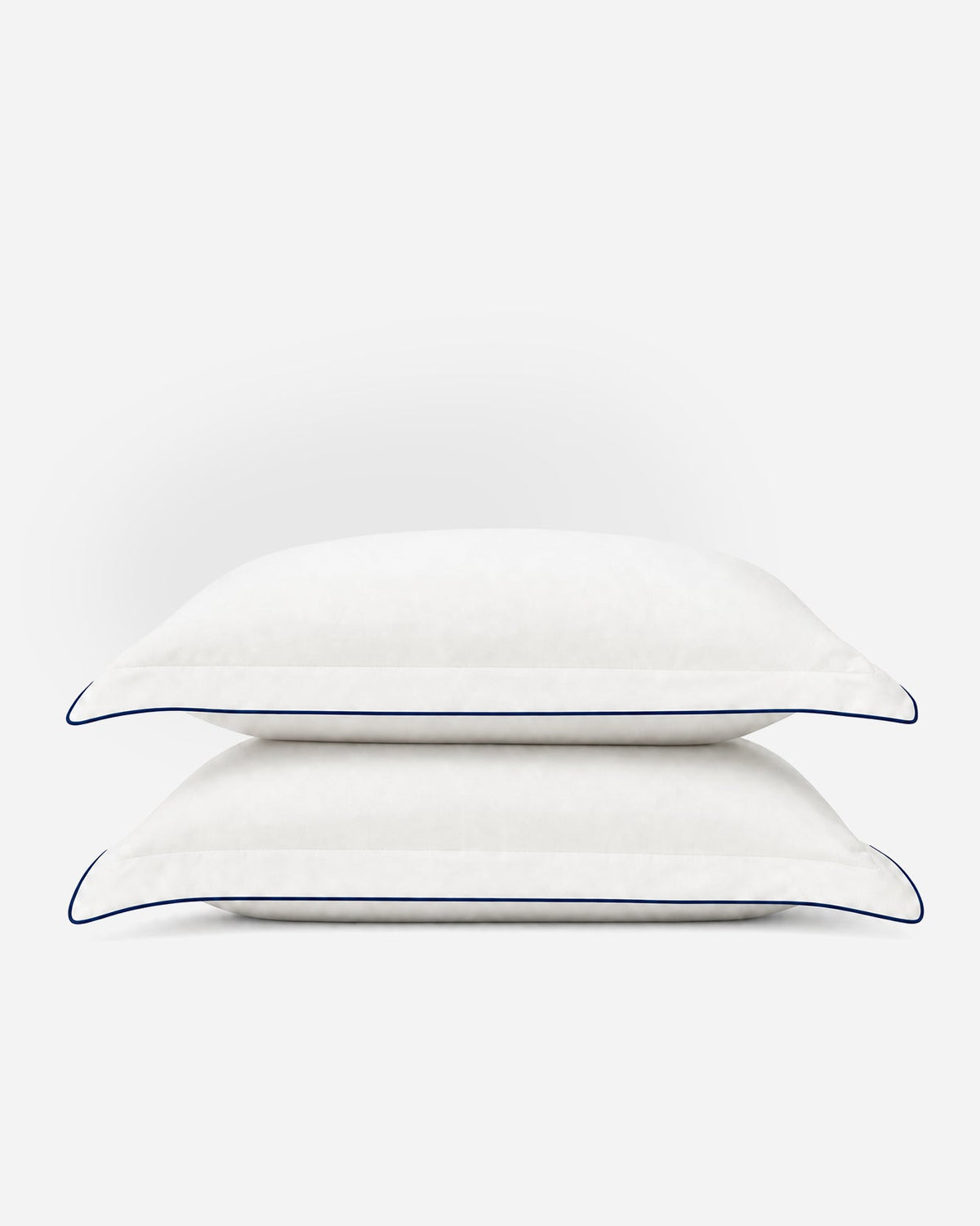 Two stacked Porto white pillowcases with midnight blue piping