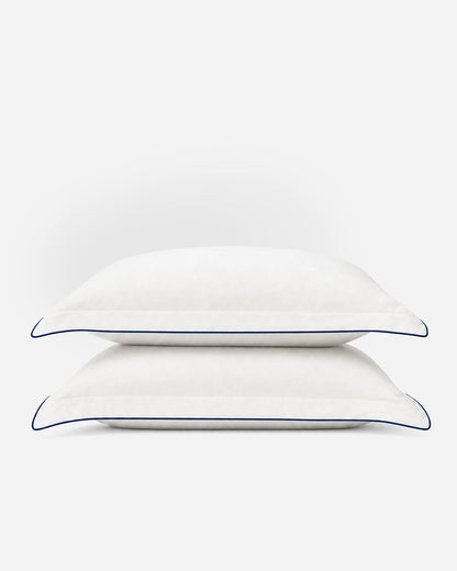 Two stacked Porto white pillowcases with midnight blue piping