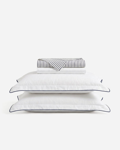 Porto sheet set with folded striped and white sheets above two blue-trimmed white pillowcases