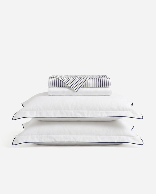 Porto sheet set with folded striped and white sheets above two blue-trimmed white pillowcases
