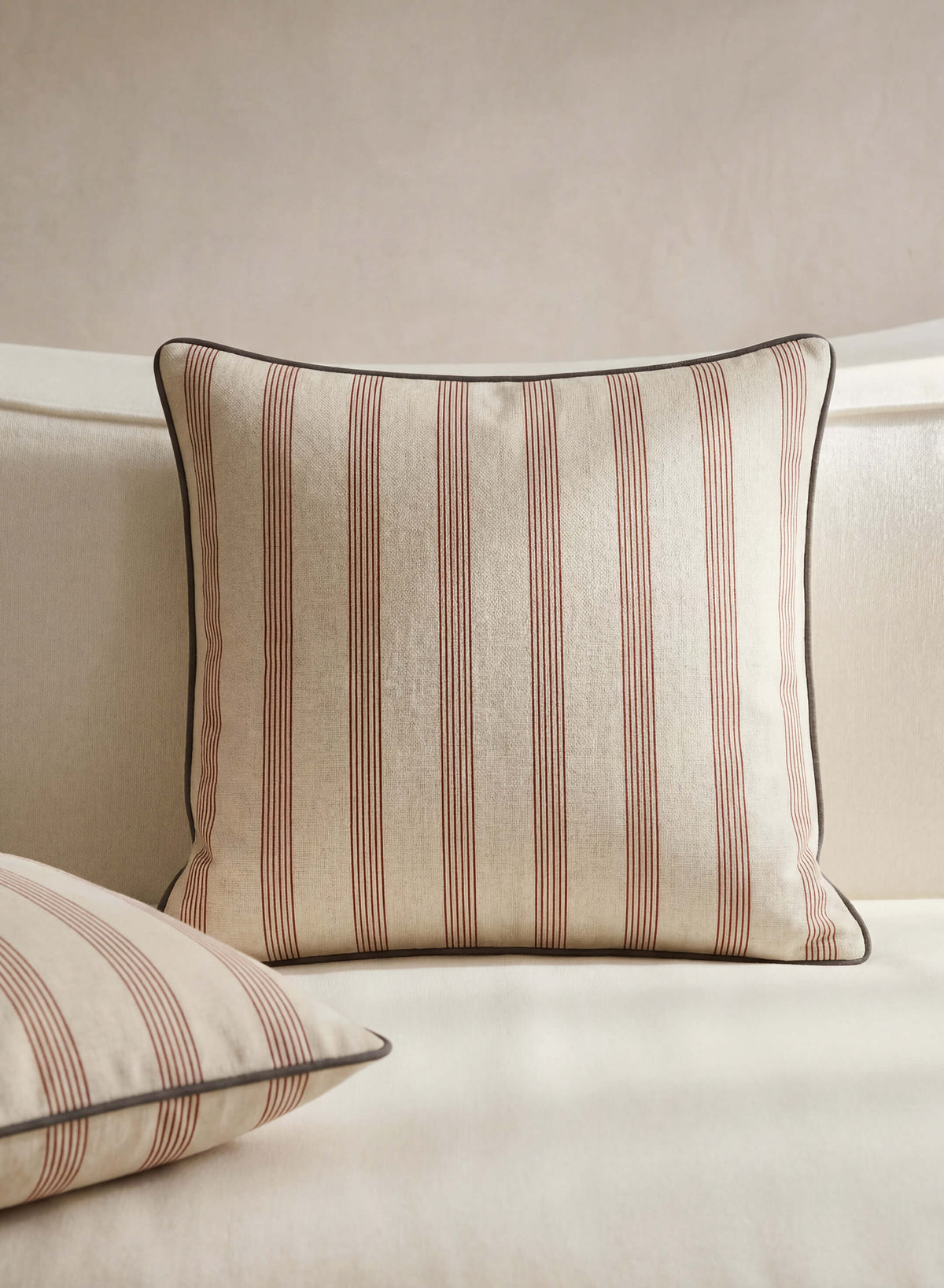 Rimini terracotta striped throw pillow styled on a cream sofa beside a matching pillow