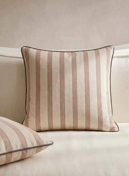 Rimini terracotta striped throw pillow styled on a cream sofa beside a matching pillow