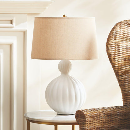 white lamp on a table next to a wicker chair